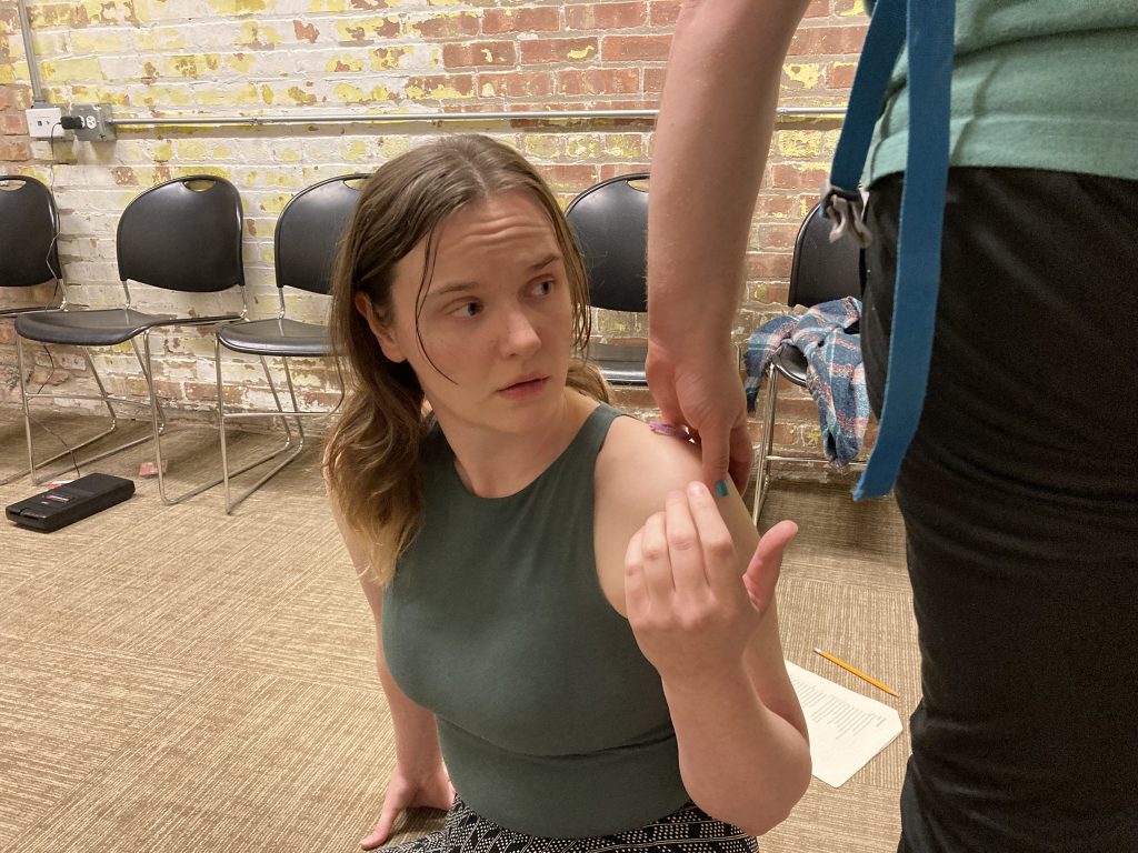 A performer watches as the other is leaving a hair tie on their shoulder while walking away.